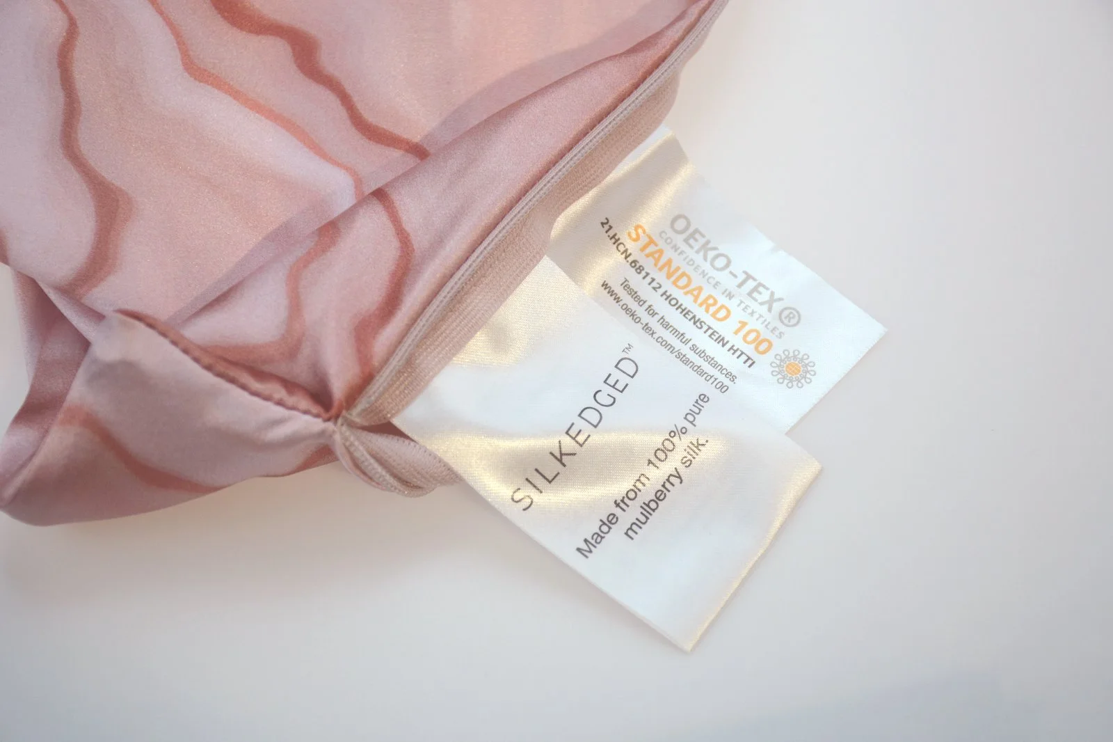 Custom satin brand and product labels beside a pink silk pillowcase zipper