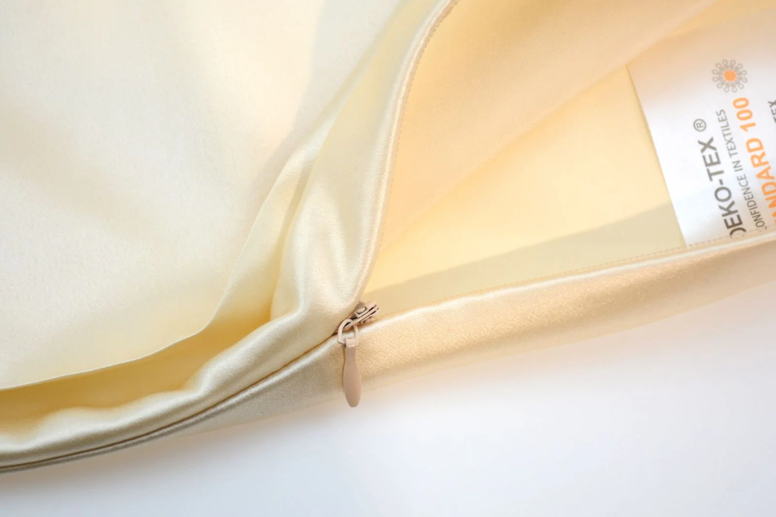 Close view of a concealed zipper and label inside a champagne silk pillowcase