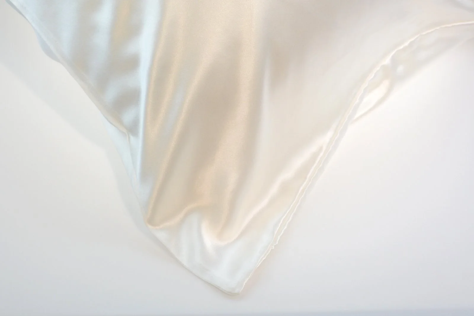 Close view of smooth ivory silk fabric and a finished pillowcase corner