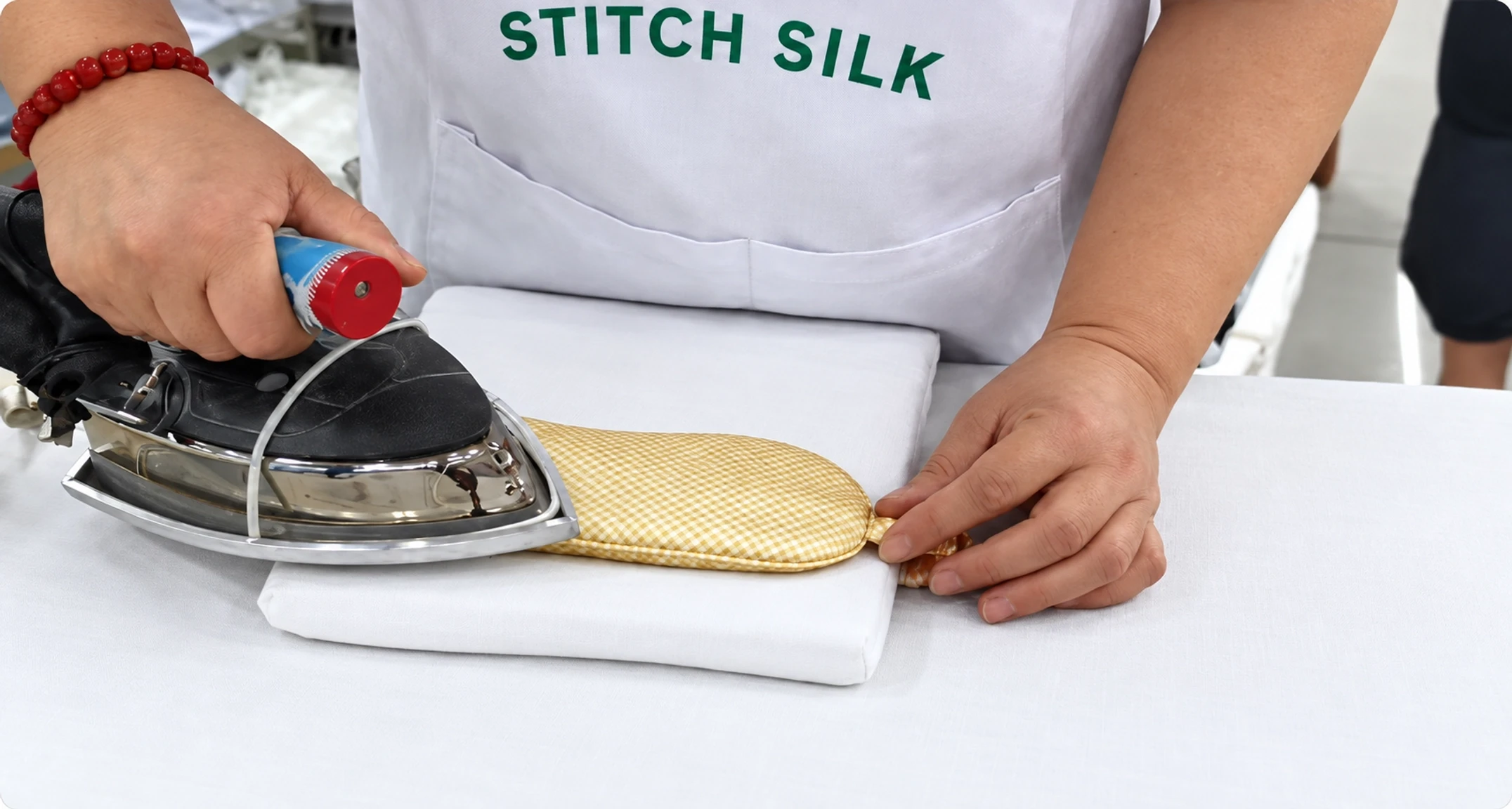 Stitch Silk factory worker steam pressing a finished silk eye mask on a padded ironing support