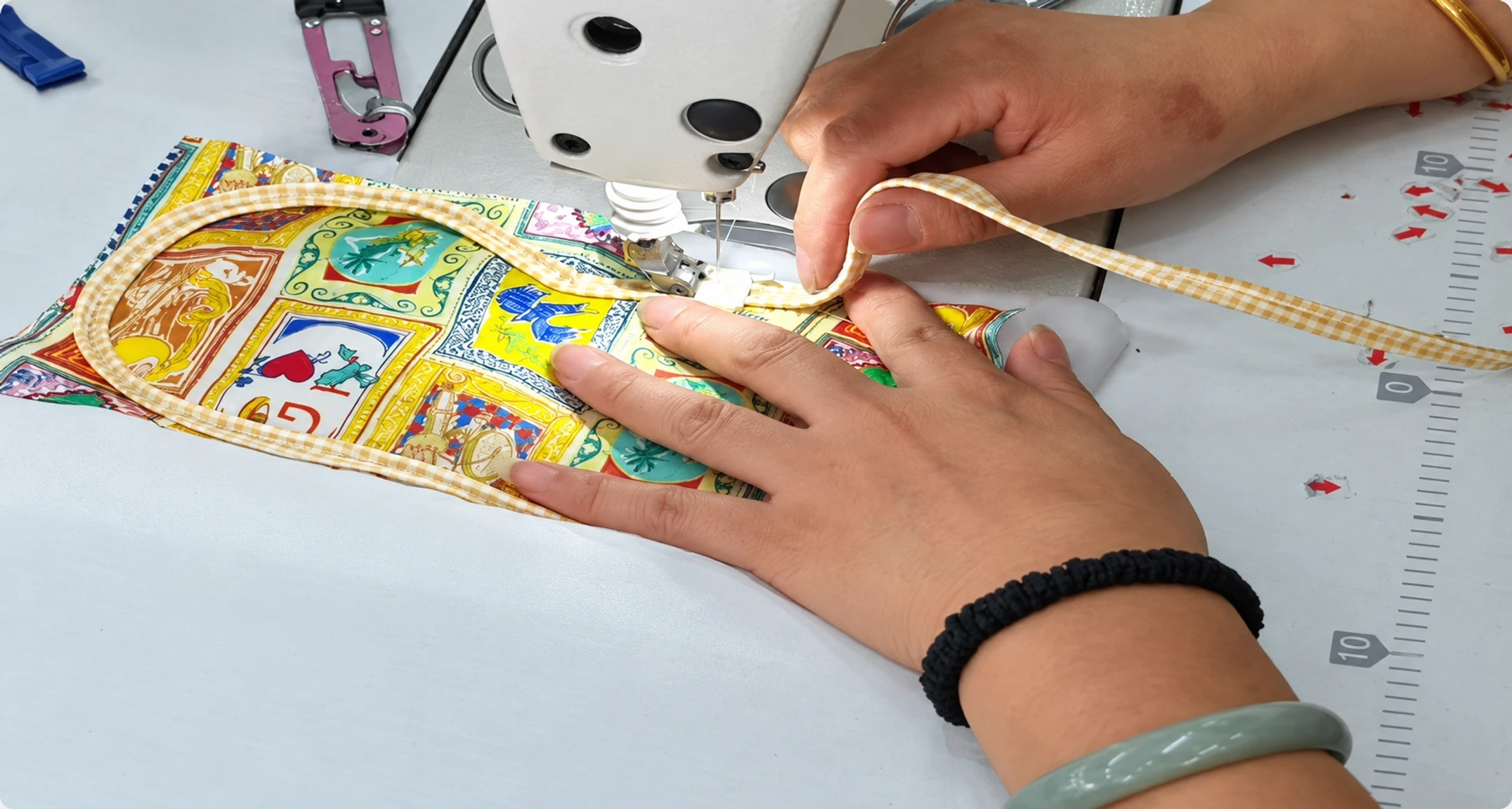 Factory worker sewing curved piping around a printed silk eye mask on an industrial sewing machine